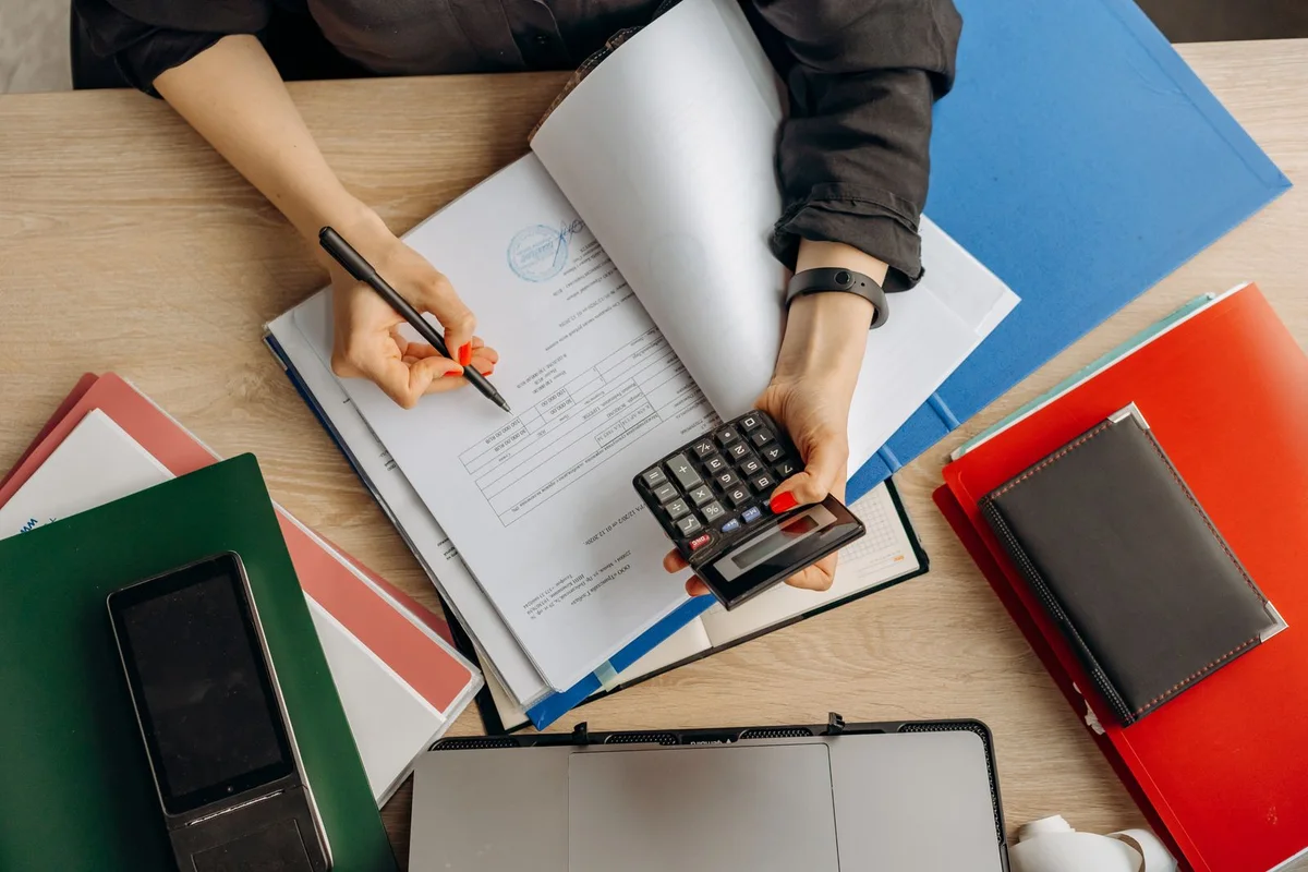 A person reviewing financial documents with a calculator and laptop
